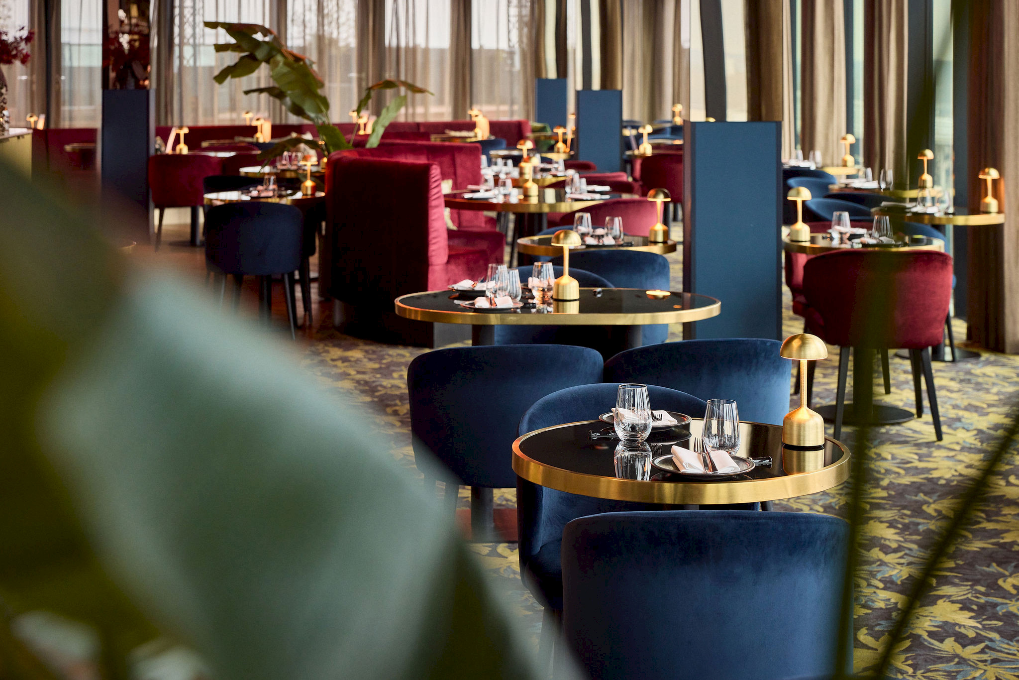 Overzicht van het Mr. Sato restaurant met afwisselend dieprode en donkerblauwe velvet fauteuils rond gouden ronde tafels