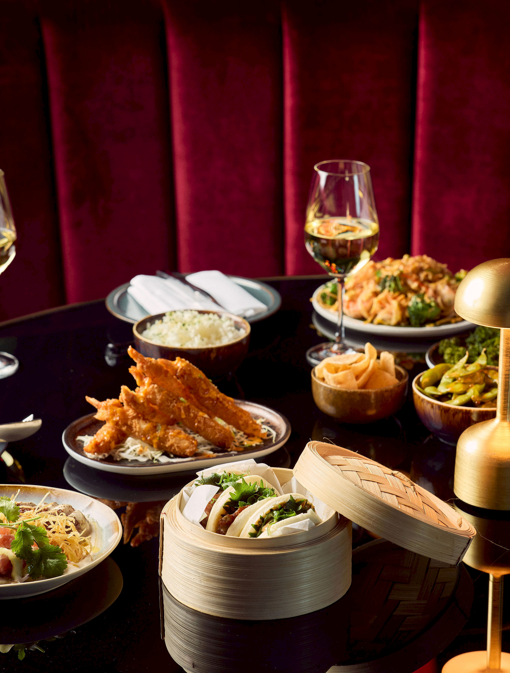 Aziatische sharing-tafel bij Mr. Sato met scampi tempura, bao buns in bamboe stomers en gyoza op een donkere tafel