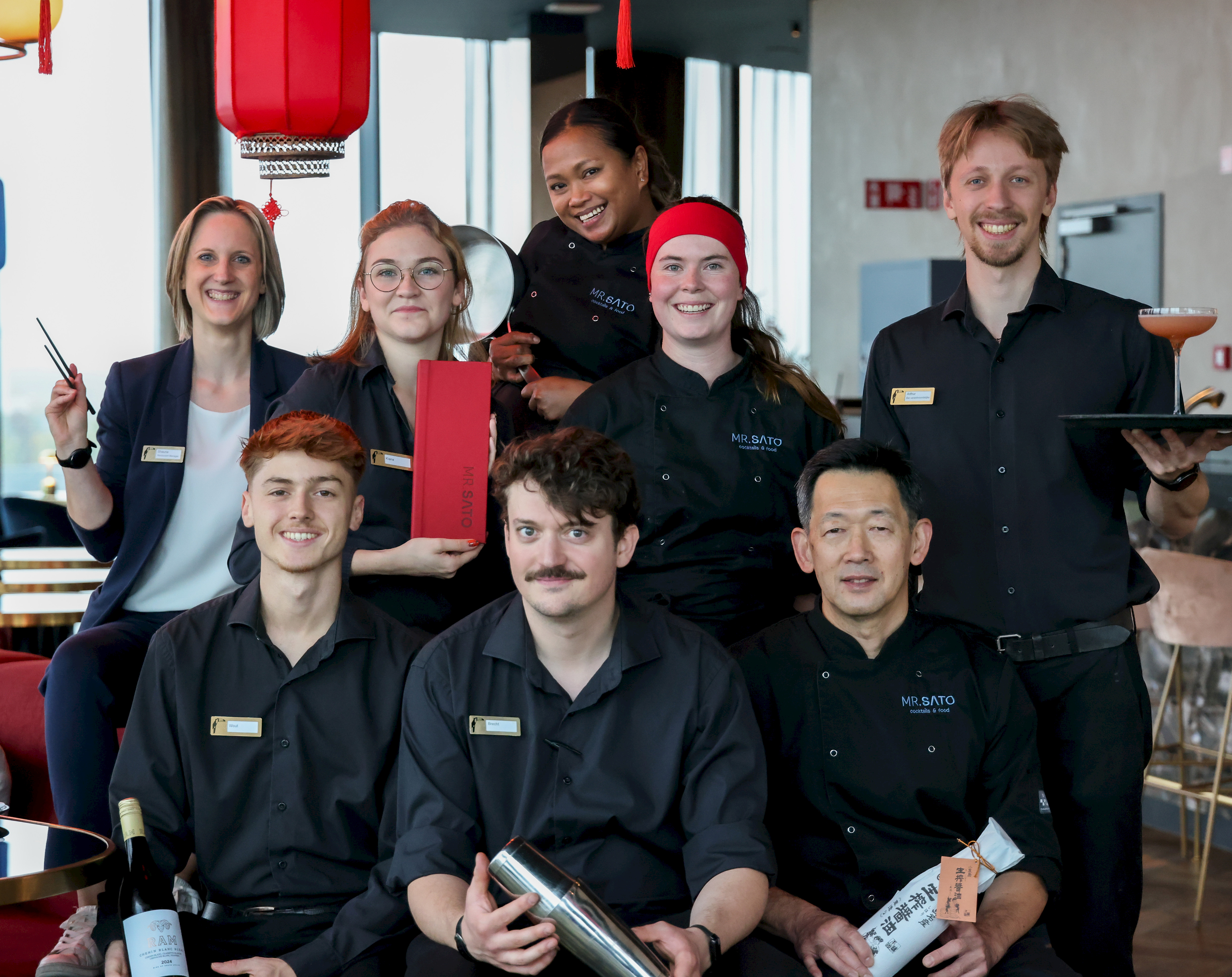 Het Mr. Sato team in zwart uniform met bordeauxrode lampion op de achtergrond - chefs, gastvrouwen en sommelier